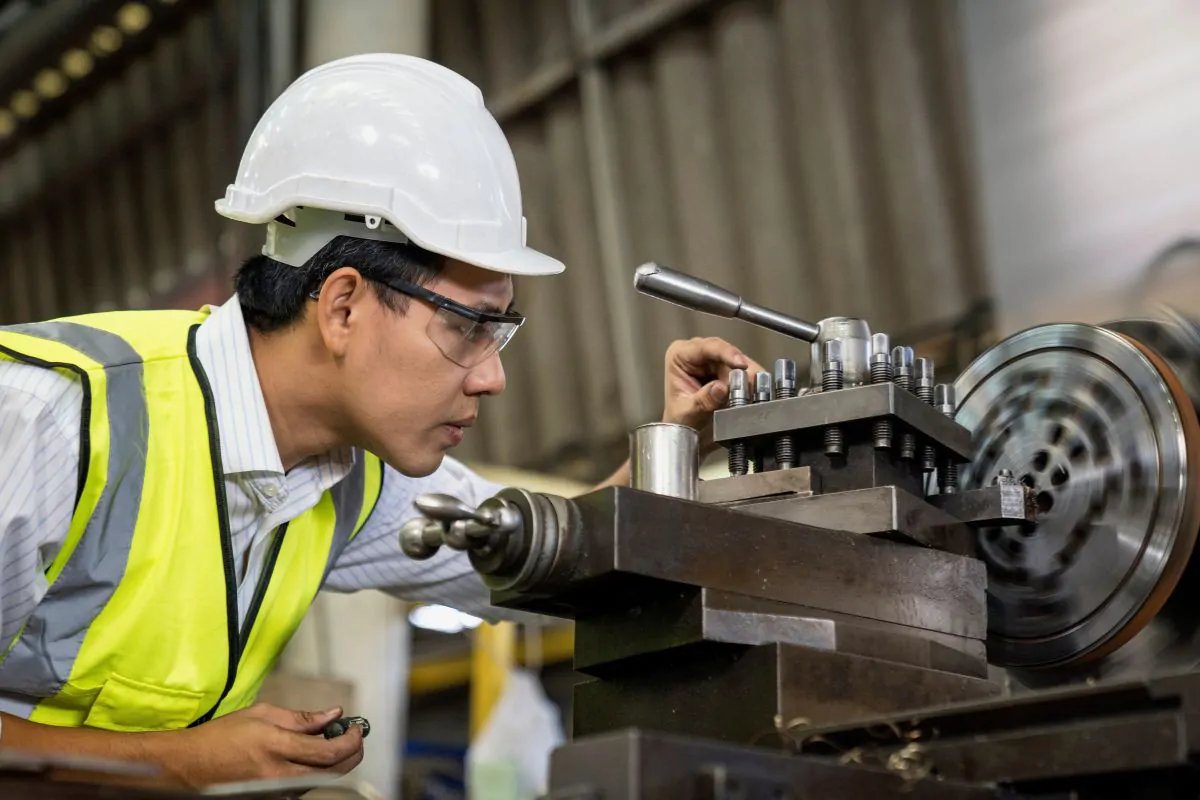 A person wearing a hard hat and working on a machineDescription automatically generated